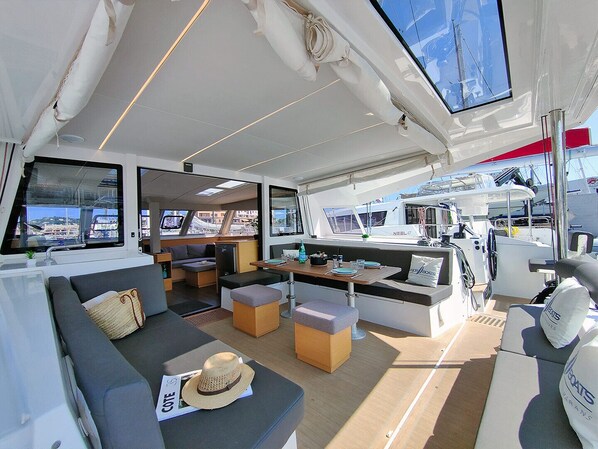 A yacht interior with a sofa, ottomans, a dining table, and a steering wheel area.