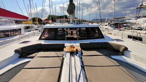 A marina with multiple sailboats docked, a covered area with seating, and a clear sky.