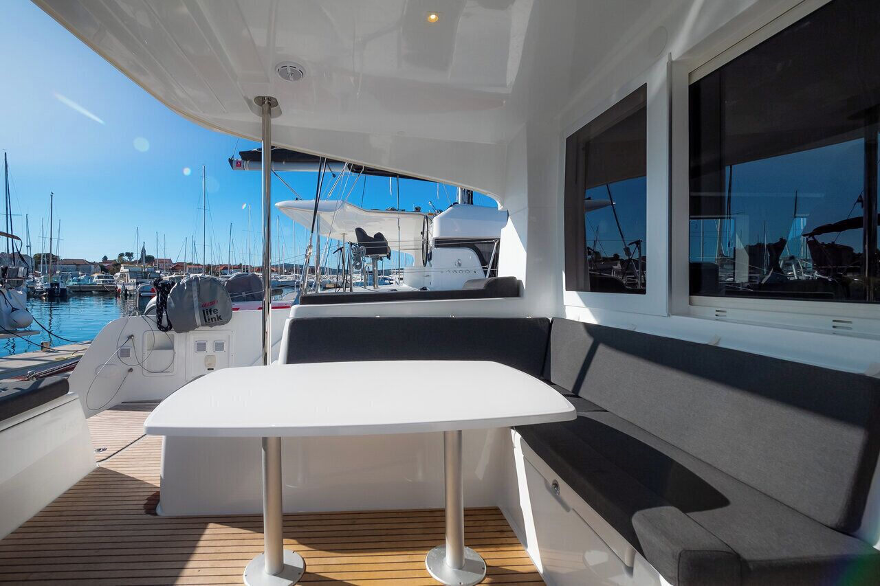 A boat deck with a table and seating, a view of the marina, and a boat in the background.