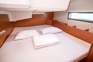 Cabine compacta com uma cama de solteiro, cabeceira de madeira, janela para iluminação natural e uma cama bem arrumada com roupa de cama branca.