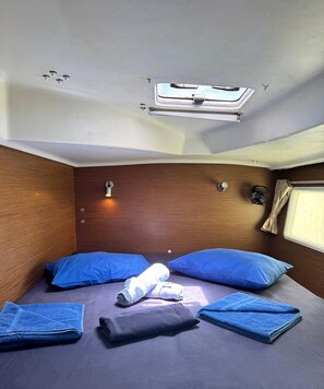 A compact room with a bed, pillows, a small table, and a window.