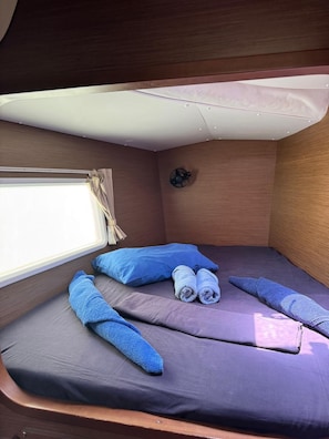 A compact cabin with a bed, a window, and a wall-mounted fan.