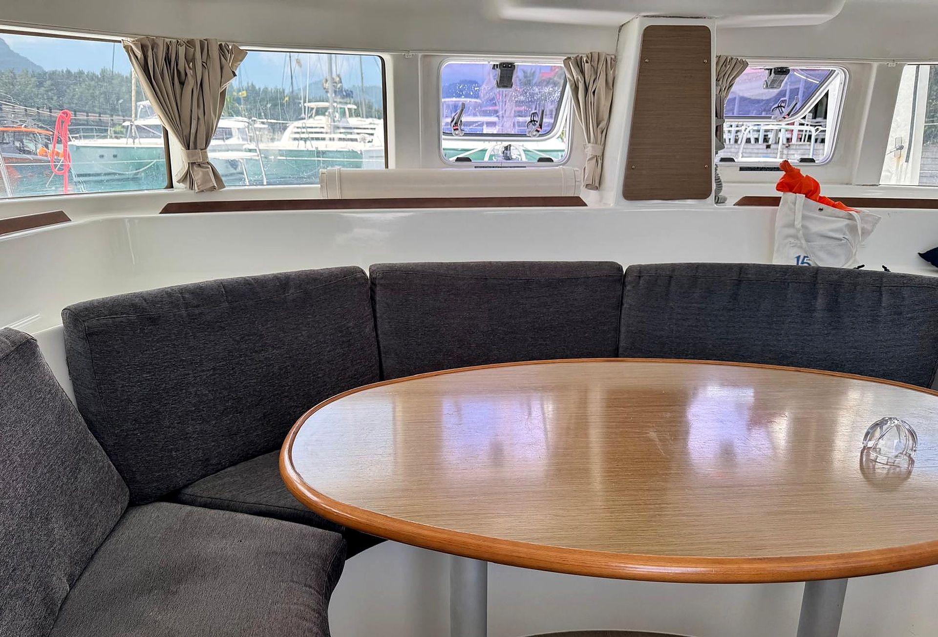 L'intérieur d'un bateau, avec une table ronde en bois et des sièges recouverts d'un tissu gris.