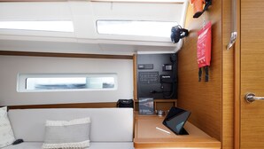 Ein kleines, kompaktes Kabinenzimmer mit einem Bett, einem kleinen Schreibtisch, einem Fenster, einer Steuerung und einer Tür.