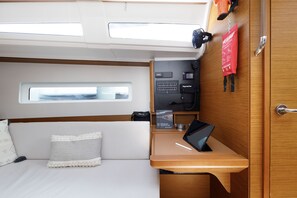 Ein kleines, kompaktes Kabinenzimmer mit einem Bett, einem kleinen Schreibtisch, einem Fenster, einer Steuerung und einer Tür.