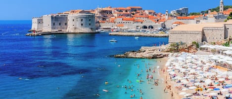 A coastal city with a historic fort, clear blue waters, and a crowded beach.