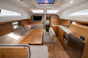 Un intérieur de bateau compact comprenant un coin repas, des sièges, un téléviseur et une cuisine équipée d’un réfrigérateur.