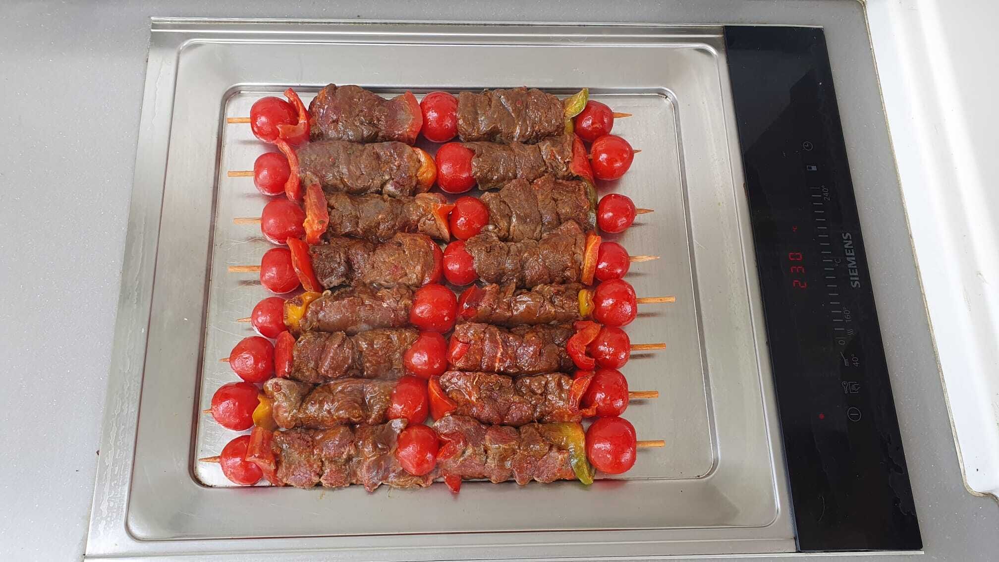 Un plateau de brochettes de viande et de tomates est posé sur un plan de travail de cuisine.