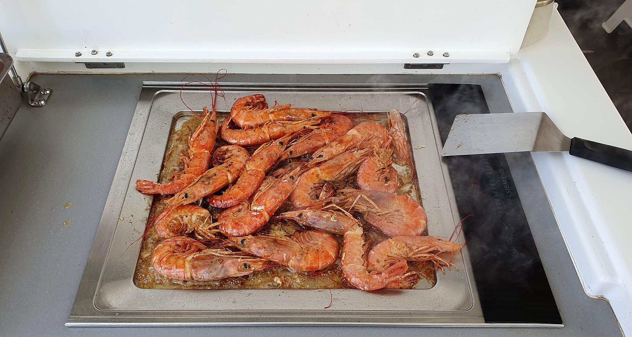 Een keuken met een schaal gekookte garnalen en een spatel.