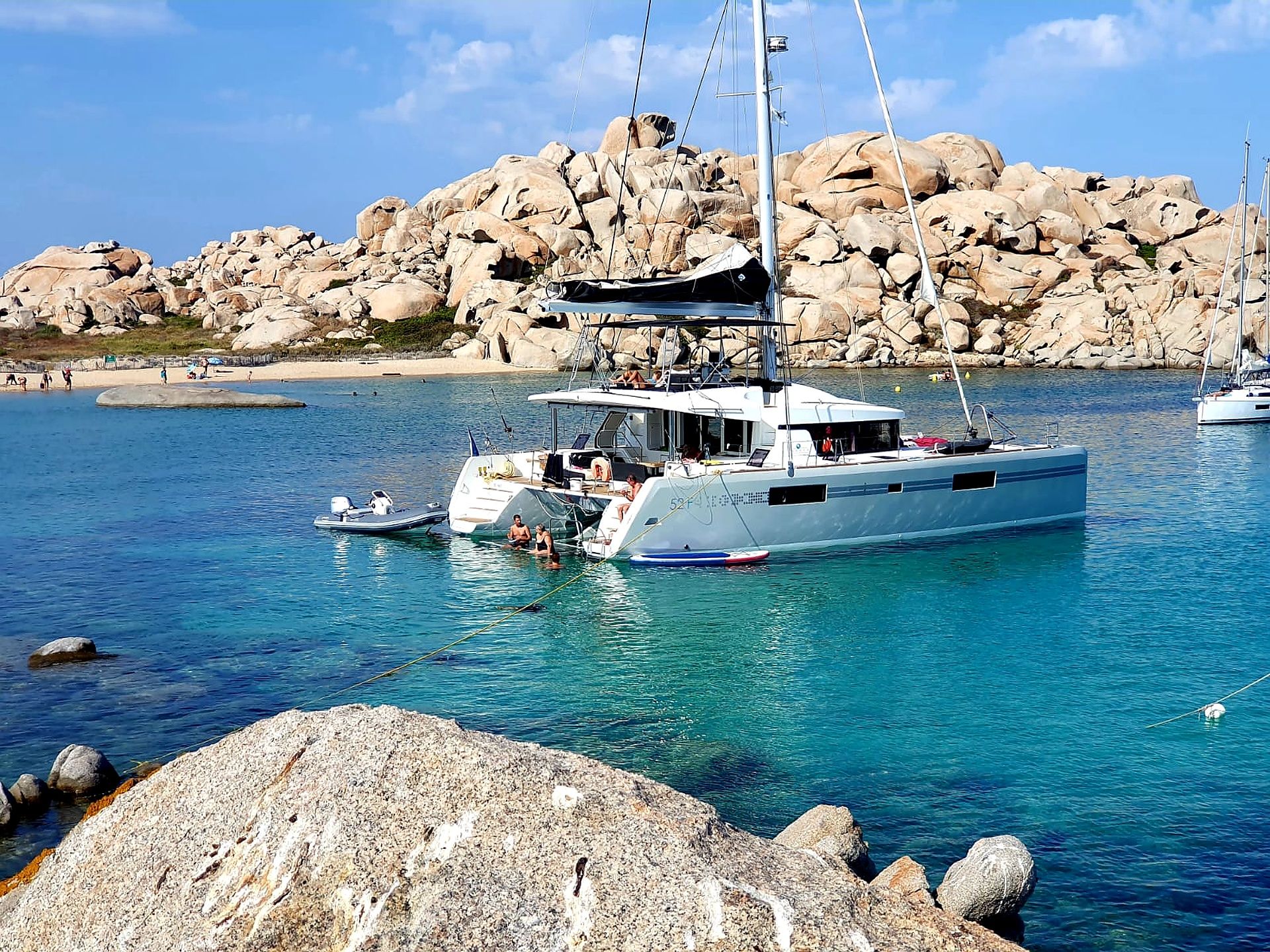 Een zeilboot afgemeerd in een rotsachtig kustgebied met helderblauw water.
