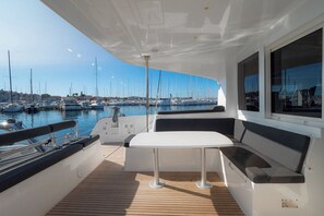 Ein Bootsdeck mit Tisch und Sitzgelegenheiten, Blick auf den Yachthafen und mehrere dort liegende Boote.