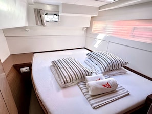 Ein Bett mit gestreiften Kissen und Handtüchern, ein kleines Fenster und eine Leuchte darüber.