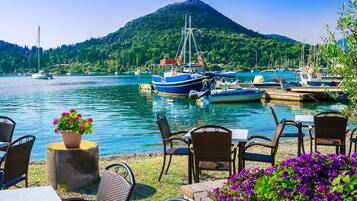 Un restaurant situé au bord de l’eau, avec une terrasse, des bateaux amarrés à proximité et une montagne en arrière-plan.