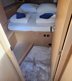 A compact bed with white linens and two blue towels, a small wooden shelf, and a grey carpeted area. - Sibenik Sun-soaked Sailing: A Luxurious Croatian Voyage (Pirovac)