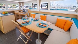 En lyxig inredning på en yacht med ett matområde, en soffa med orange kuddar och utsikt över hamnen.