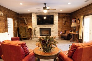 A living room with leather sofas, a fireplace, a television mounted on a stone wall, and a ceiling fan.