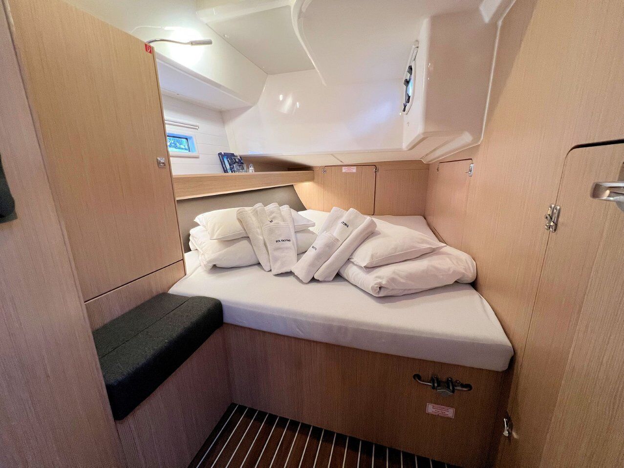 Una cabaña compacta y bien iluminada con cama, armarios para guardar objetos y un ventanal pequeño.