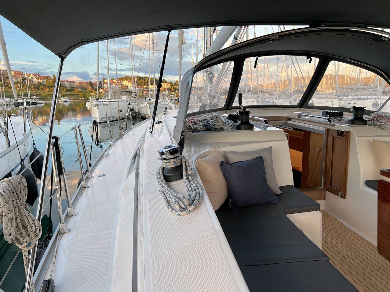 Das Deck eines Segelboots mit gepolsterten Sitzgelegenheiten, einem Mast und anderen Booten im Hintergrund.