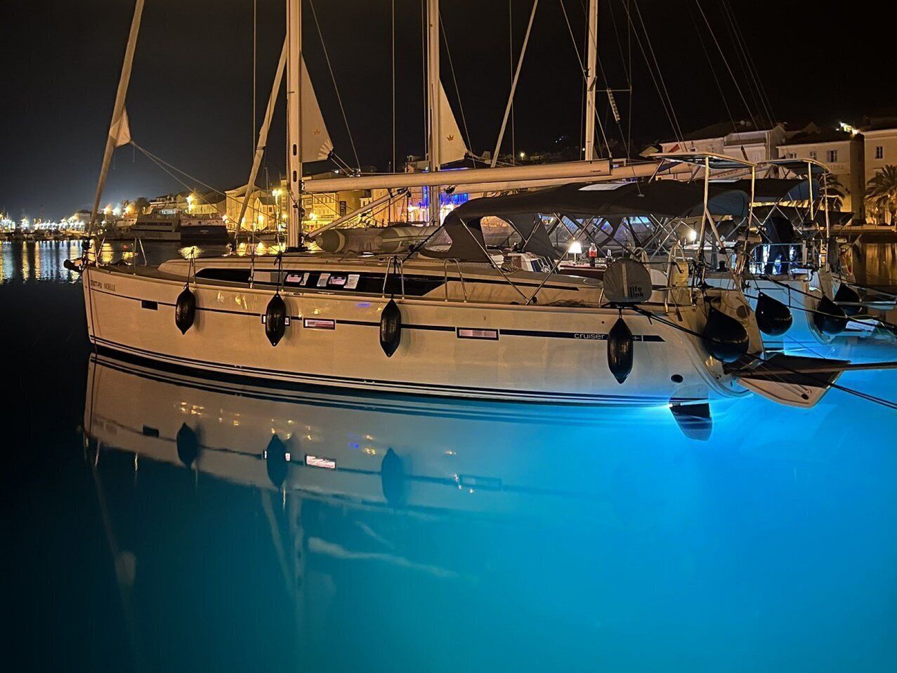 Een zeiljacht afgemeerd in een jachthaven, met een rustig wateroppervlak dat het schip weerspiegelt.