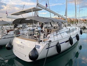 A white yacht named 'NOELLE' docked at a marina with other boats, a covered deck, and a cityscape in the background. - Sun-Kissed Sailing Adventure in Istria, Croatia (Pula)