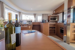 A modern kitchen with a microwave, oven, and a small refrigerator. There are two bottles on the counter, and a book is also visible. - Sun-Kissed Sailing Adventure in Zadar, Croatia (Biograd na moru)