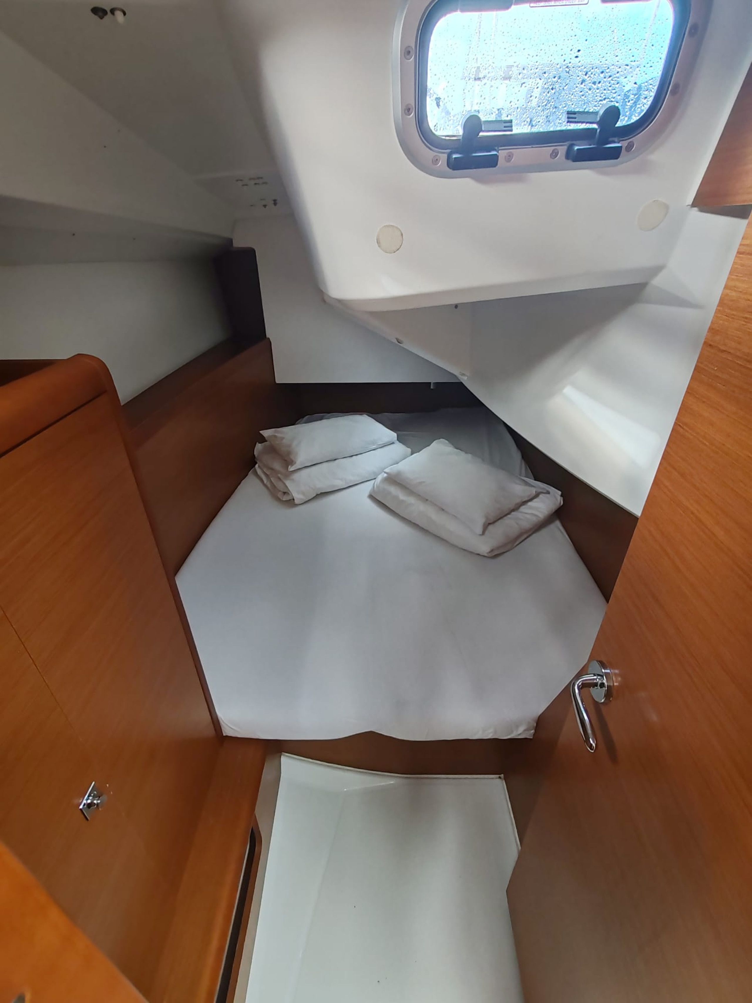 Une petite cabine avec une petite fenêtre, un banc en bois et un lit bien fait, agrémenté de serviettes.