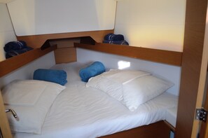 A bunk bed with white bedding and blue pillows, a wooden headboard, and a small overhead shelf.
