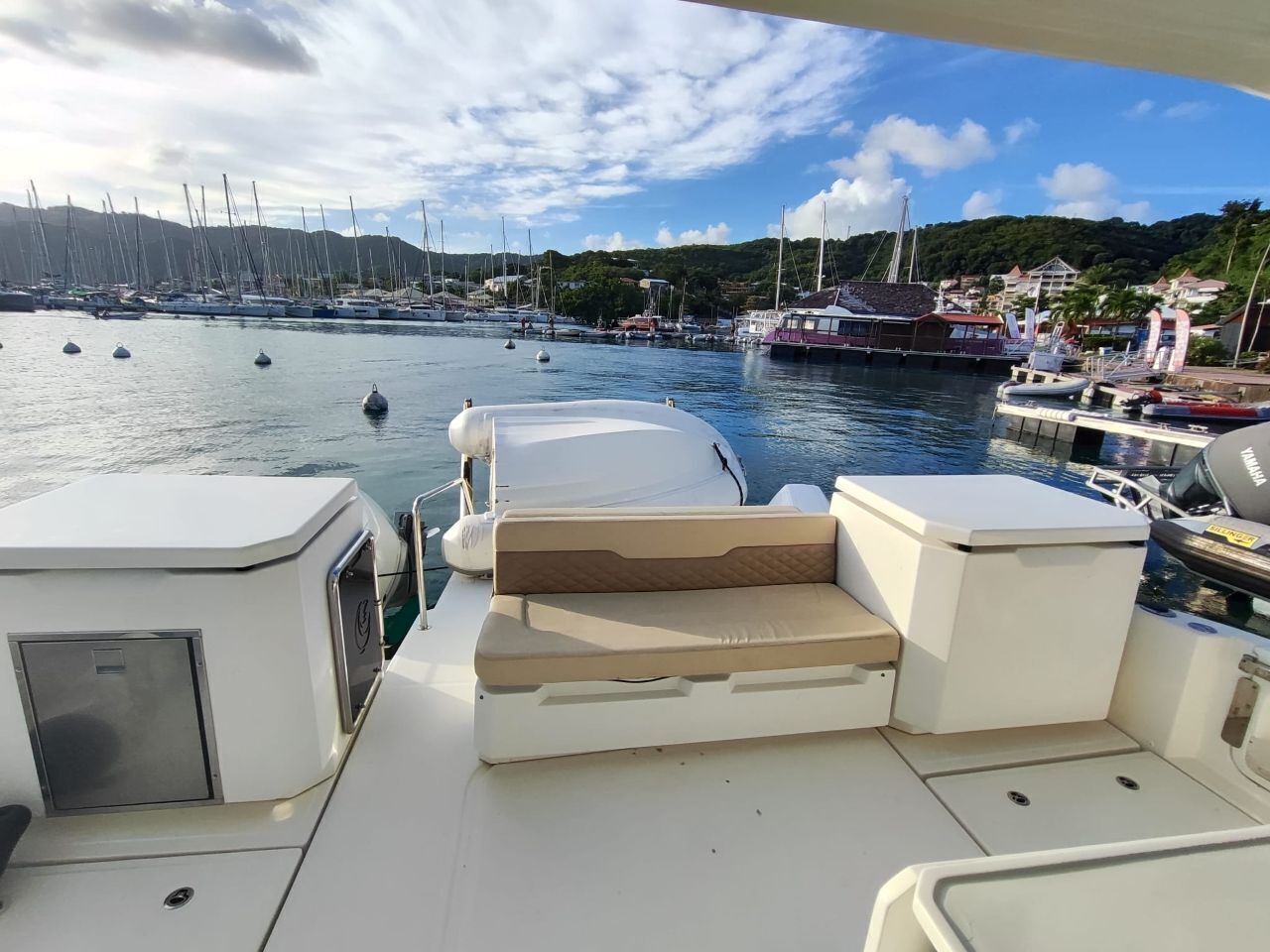 Cubierta de barco con asientos, un motor fueraborda Yamaha y un puerto deportivo con barcos y casas al fondo.