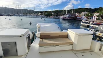 Cubierta de barco con asientos, un motor fueraborda Yamaha y un puerto deportivo con barcos y casas al fondo.