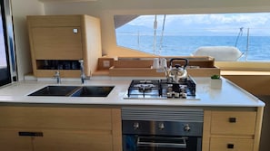 A compact galley kitchen with a sink, stove, and storage cabinets, overlooking the sea. - Sun-Kissed Sailing Adventure in the Ionian Islands (Kallithea)