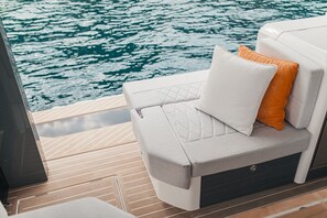 Ein Bootsdeck mit einer gepolsterten Sitzecke und Blick auf das Wasser, mit Holzboden.