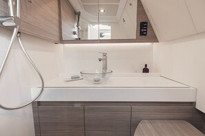 Een moderne badkamer met een glazen wastafelbak, een handdouche en een spiegel boven de wastafel.