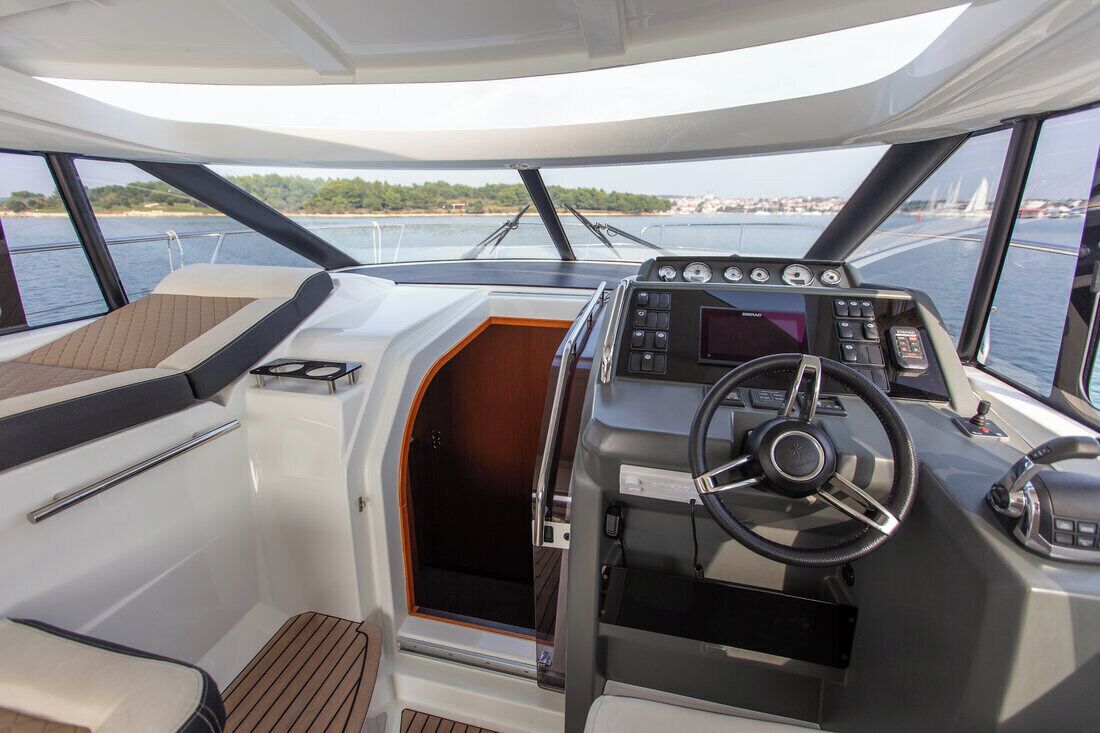 Bootinterieur met stuurwiel, bedieningspaneel en ramen met uitzicht op het water.