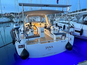 Iachta blanca anomenada 'JANA PULA' amarrada en una marineda, amb altres embarcacions, que inclou una cabina, timó i un nom al proa.