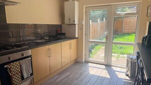 Eine moderne Küche mit Gasherd, Edelstahlgeräten, Holzschränken und einer Glastür, die in einen Garten führt.