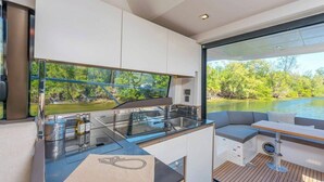 Een modern interieur van een boot met een keukenhoek, zitplaatsen en uitzicht op een meer.