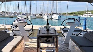En overdækket terrasse med siddepladser, et bord og udsigt til en lysthavn med både.
