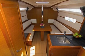 A compact boat interior with a dining table, bench seating, a small kitchen area with a sink, and a window. - Sun-Kissed Sailing Adventure in Split, Croatia (Split)