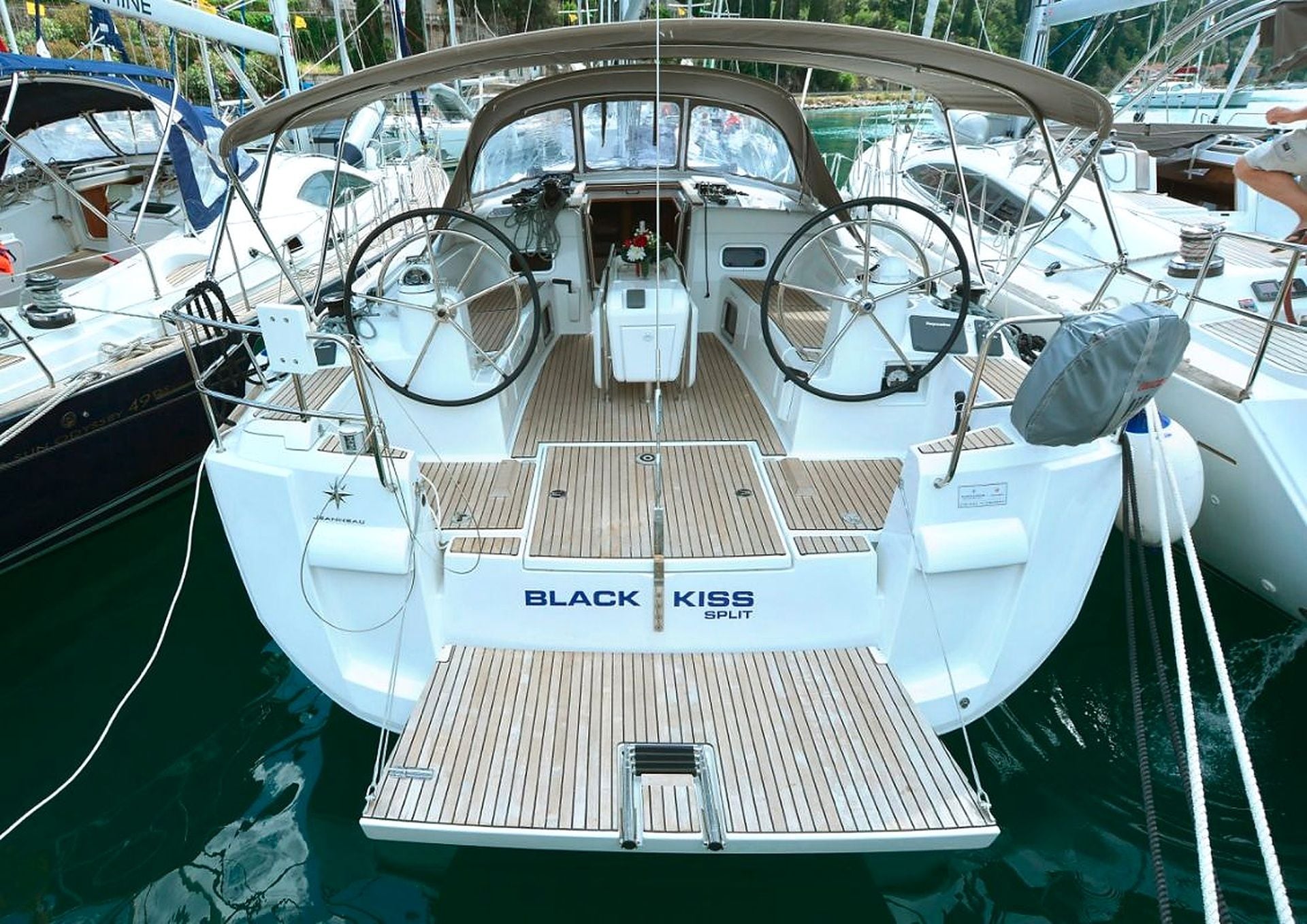 Ein Boot namens BLACK KISS SPLIT liegt in einer Marina mit einem Holzboden und einem Steuerrad vor Anker.