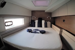 Habitación pequeña y bien iluminada con una cama, un ventanal y un cabecero con compartimentos de almacenamiento.