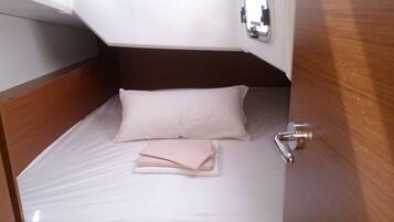A small, neatly made bed with a white mattress and a single pillow, a folded towel, and a wooden headboard.