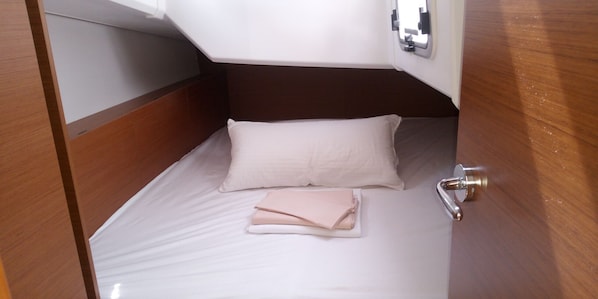 A small, neatly made bed with a white mattress and a single pillow, a folded towel, and a wooden headboard.