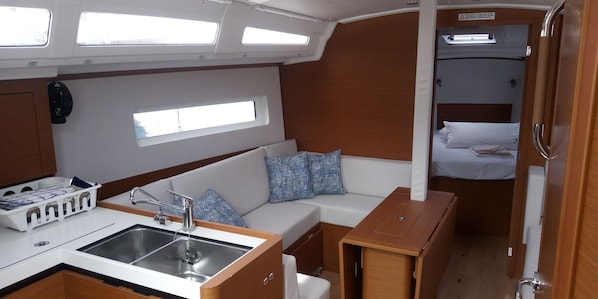 A compact galley with a sink, a small wooden table, and a sofa with patterned cushions.