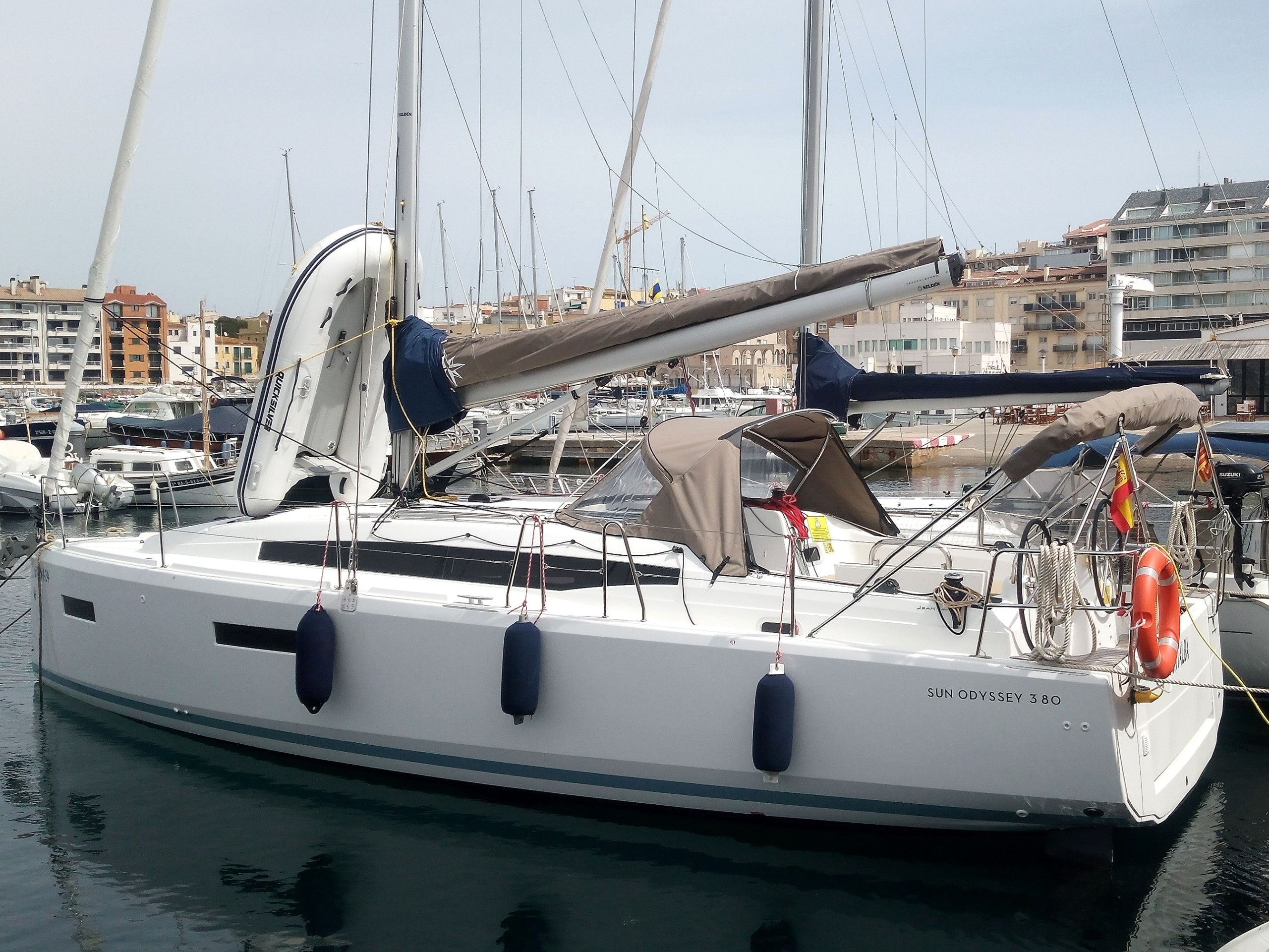 A sailboat docked at a marina with multiple masts, a cabin, and a lifebuoy.