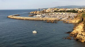 A coastal marina with boats, a rocky breakwater, and a town in the background.