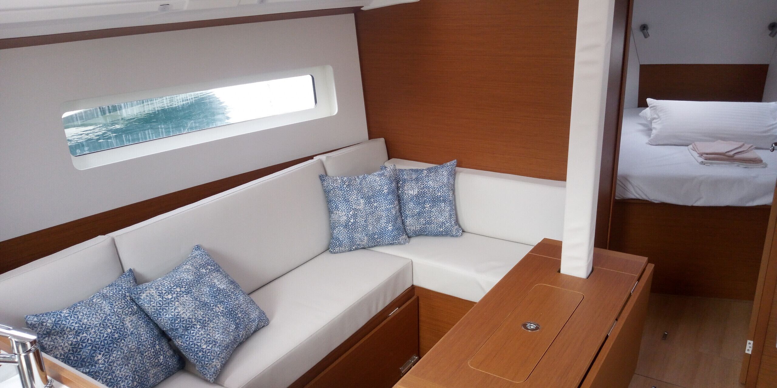 Una cabaña con un sofá blanco, almohadones estampados, una mesa de madera y una cama pequeña con ropa de cama blanca.