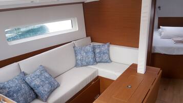 Una cabaña con un sofá blanco, almohadones estampados, una mesa de madera y una cama pequeña con ropa de cama blanca.