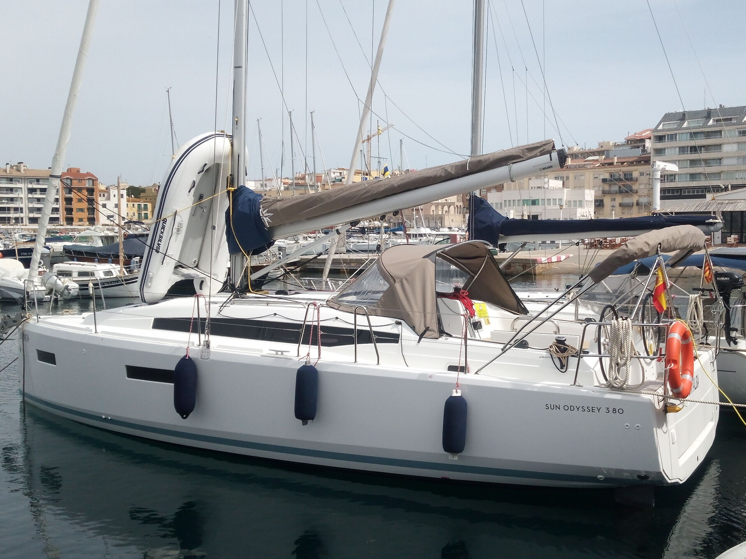 A sailboat docked at a marina with multiple masts, a covered deck area, and a visible lifebuoy.