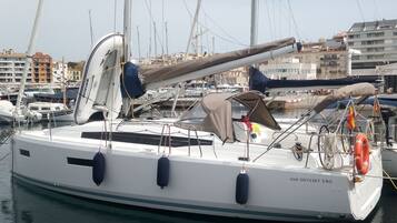 A sailboat docked at a marina with multiple masts, a covered deck area, and a visible lifebuoy.