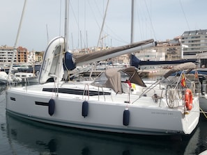 A sailboat docked at a marina with multiple masts, a covered deck area, and a visible lifebuoy.